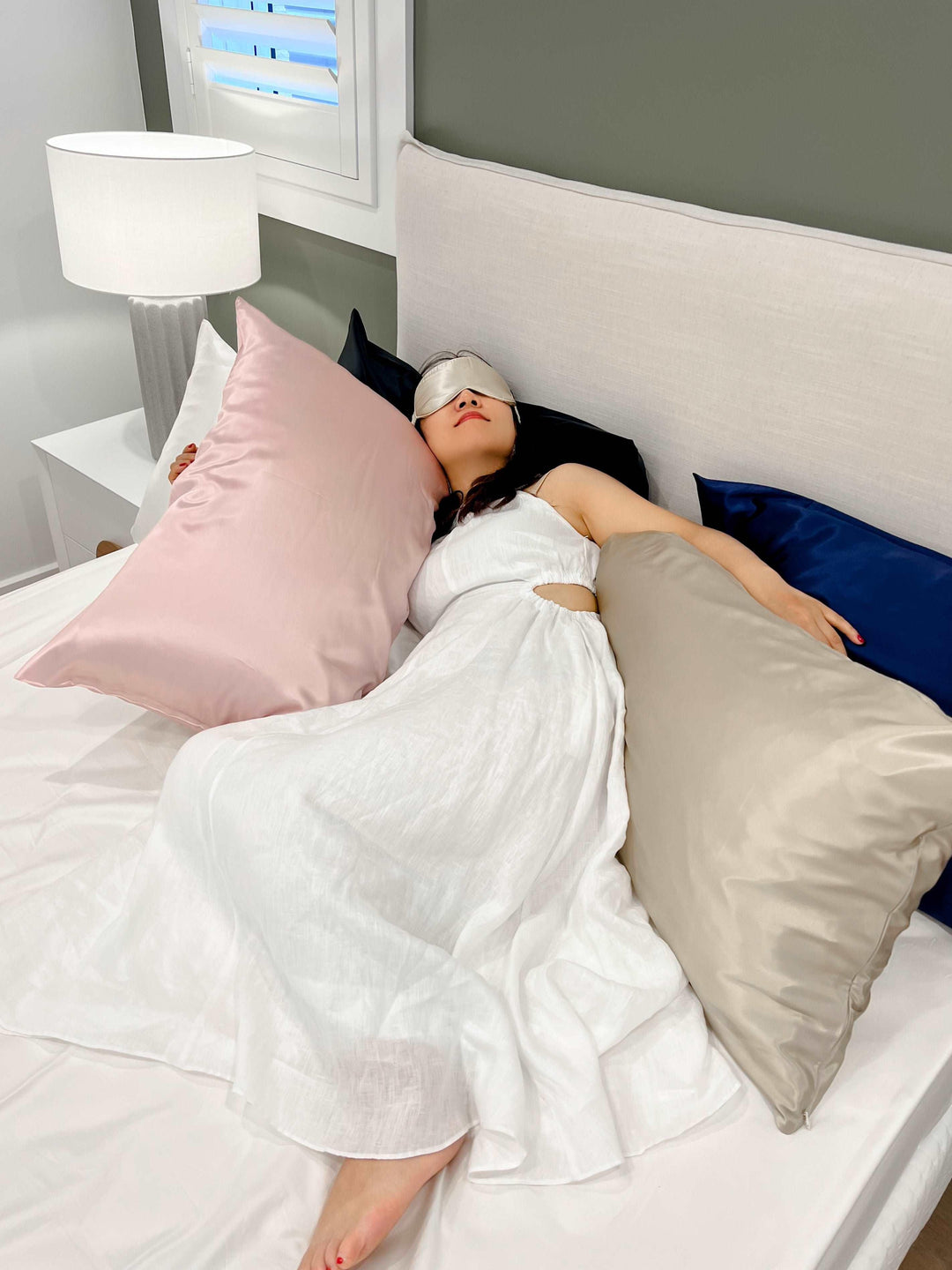 A woman in a white dress lying on a bed with Champagne Moon Flower silk linens