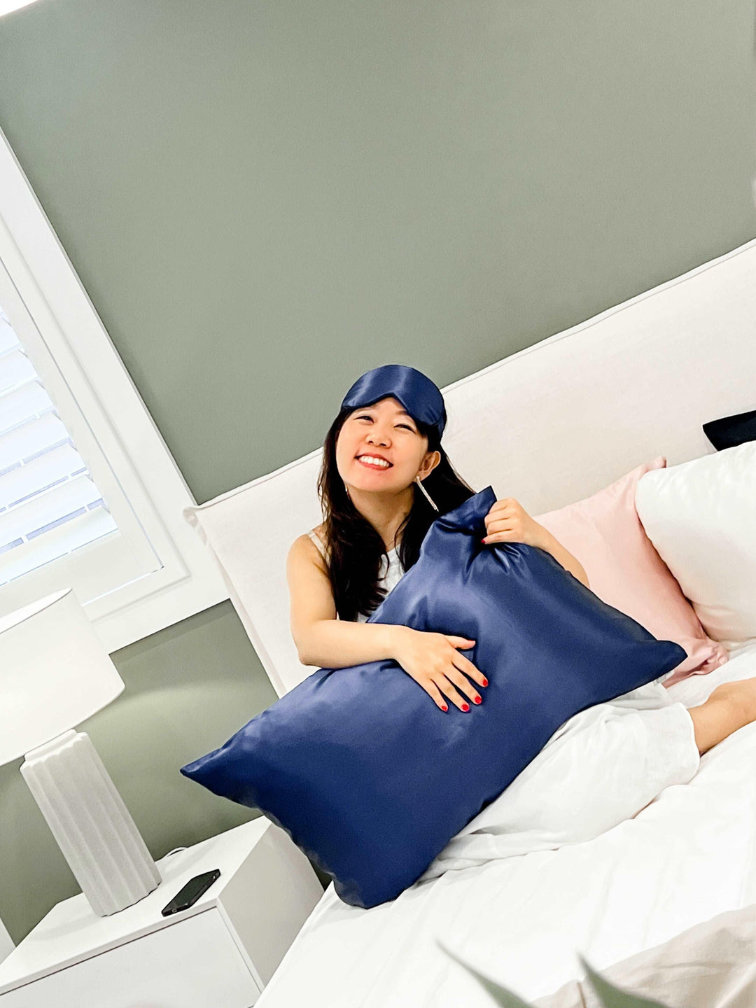 Woman seated on a bed with the navy blue silk pillow from the gift set