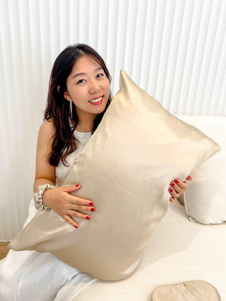 Woman presenting a champagne silk sleep mask with a shimmering Champagne pillowcase