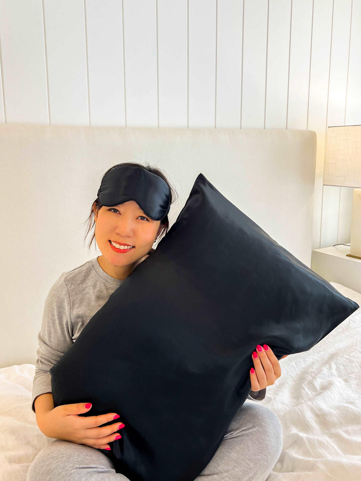 A woman reclining on a bed, showcasing the black queen silk pillowcase