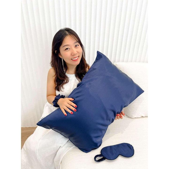 Woman relaxing on a couch holding a navy blue silk pillow from the silk gift set