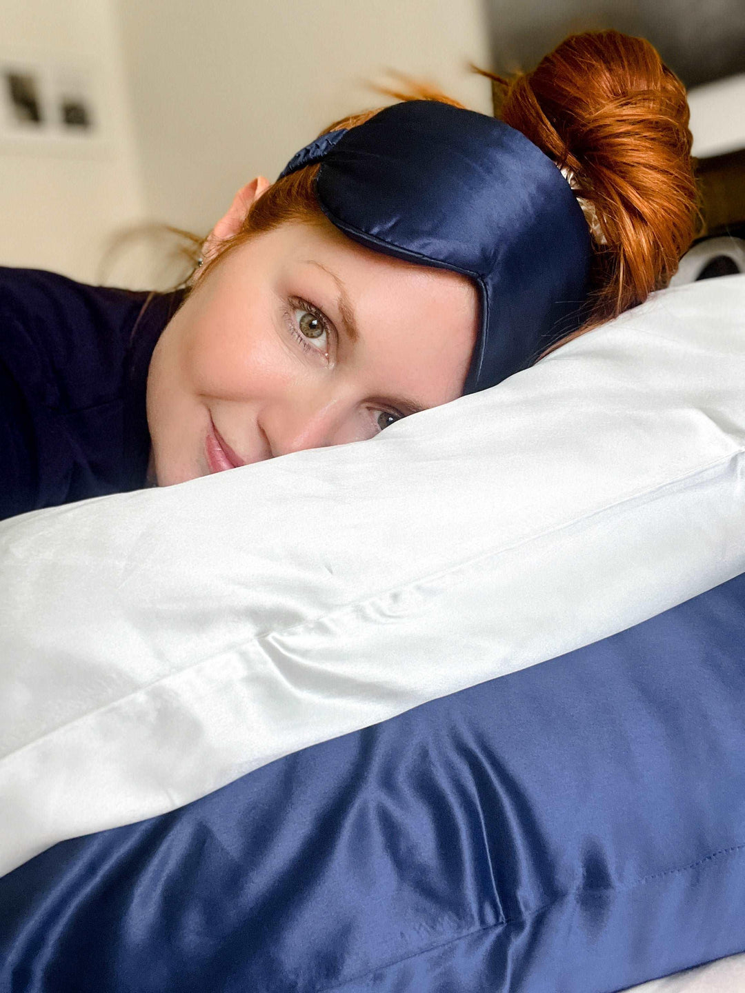 Navy blue silk sleep mask on a silk pillow beside a sleeping woman