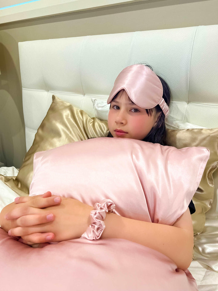 Child resting on a bed with the Pink Queen silk pillowcase