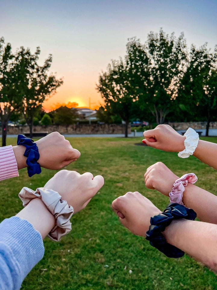 Group of friends showing off their champagne silk hair scrunchies outdoors