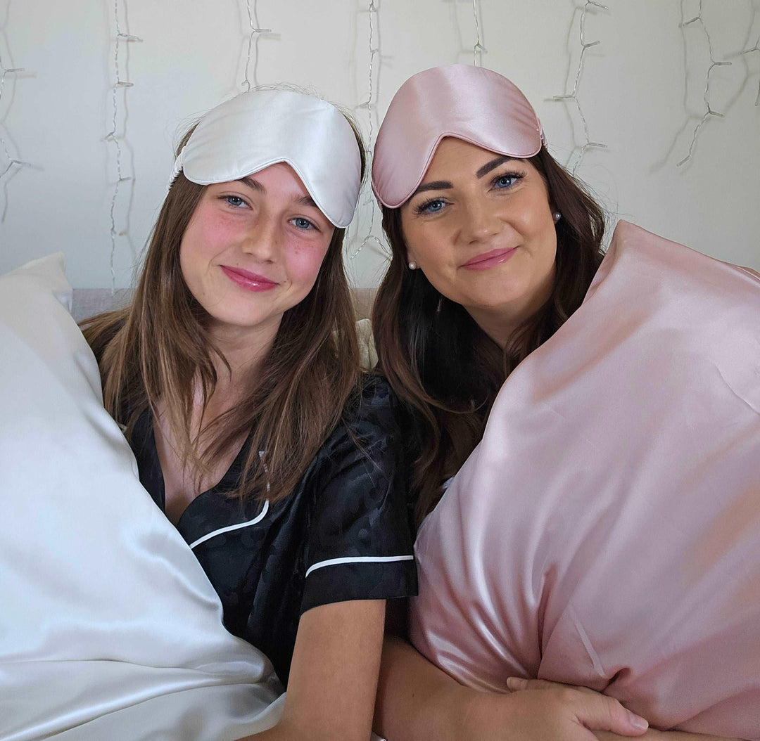 A mother and daughter showcasing pink and white silk sleep masks in a lifestyle setting