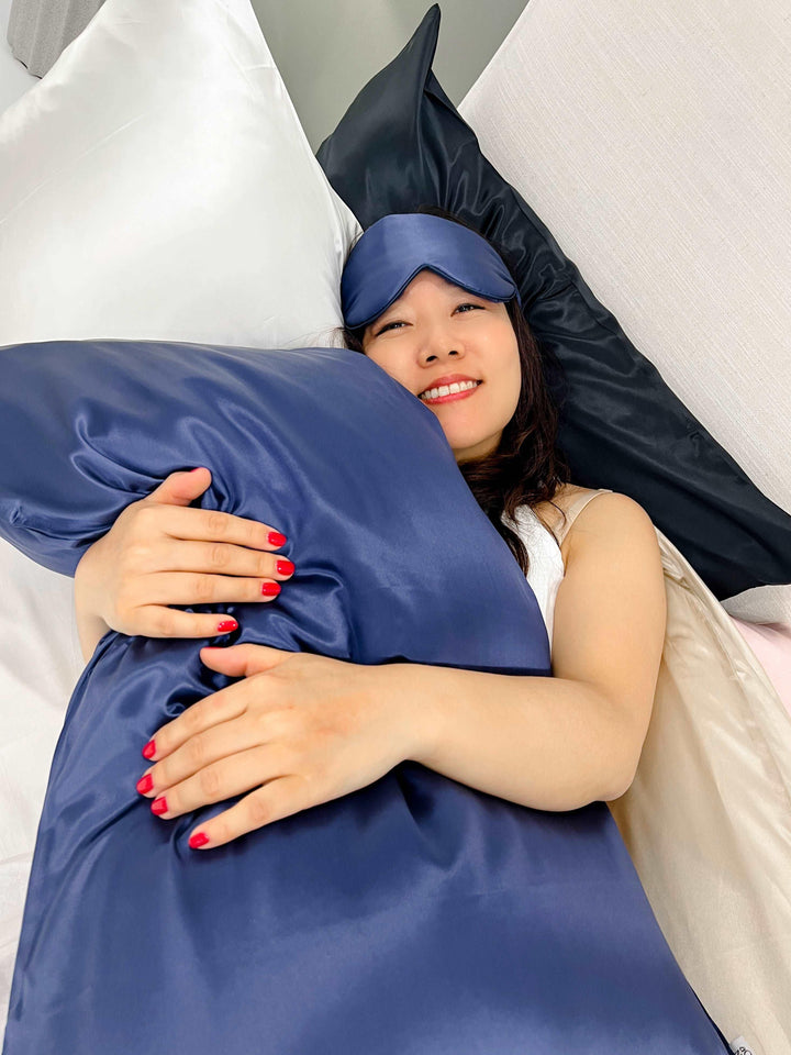 Woman resting in bed with the navy blue silk pillow of the gift set