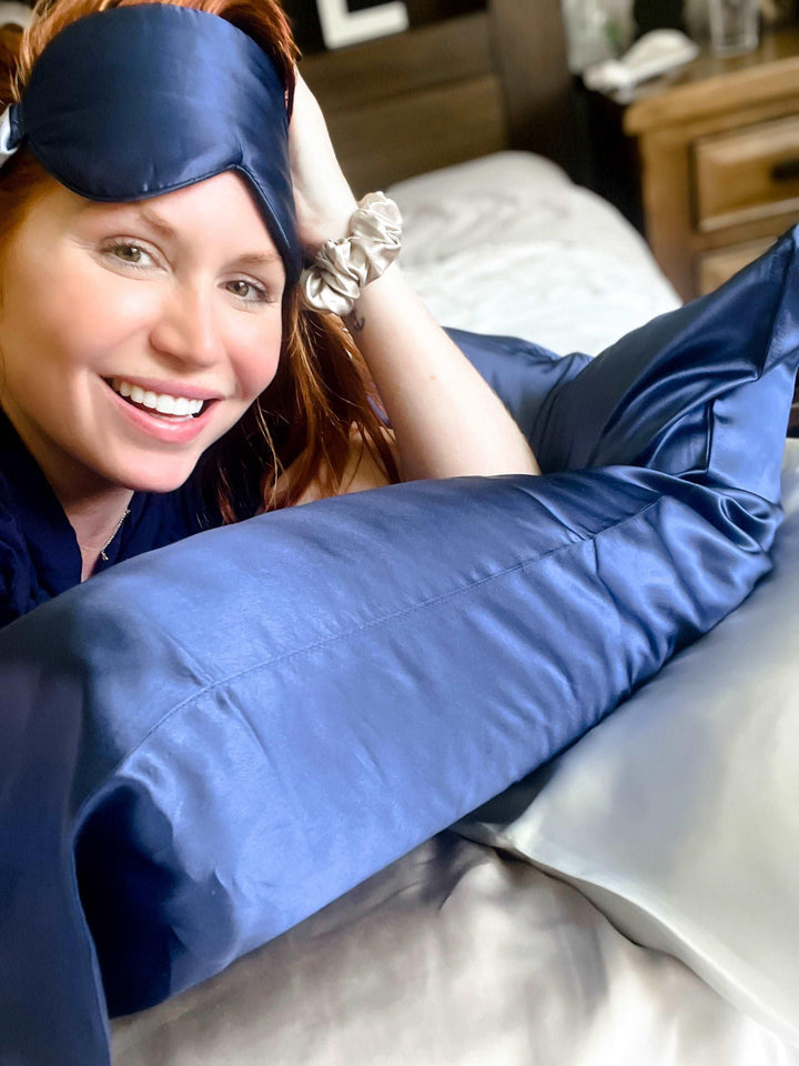 Smiling woman lying on a bed with the navy blue silk pillow from the set