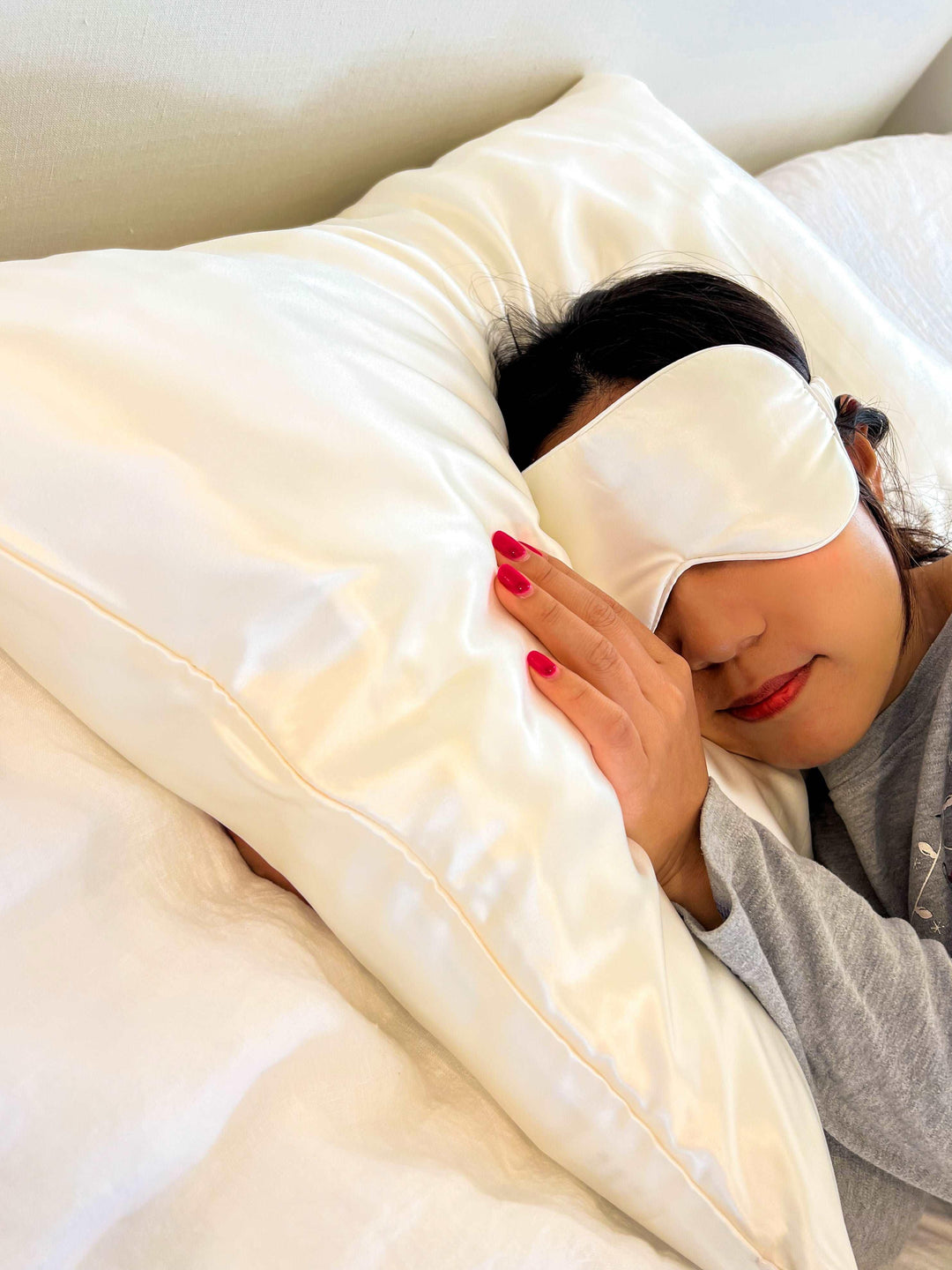 A woman sleeps with a White Queen silk pillowcase and a matching white eye mask,  perfect for hair care and skin.