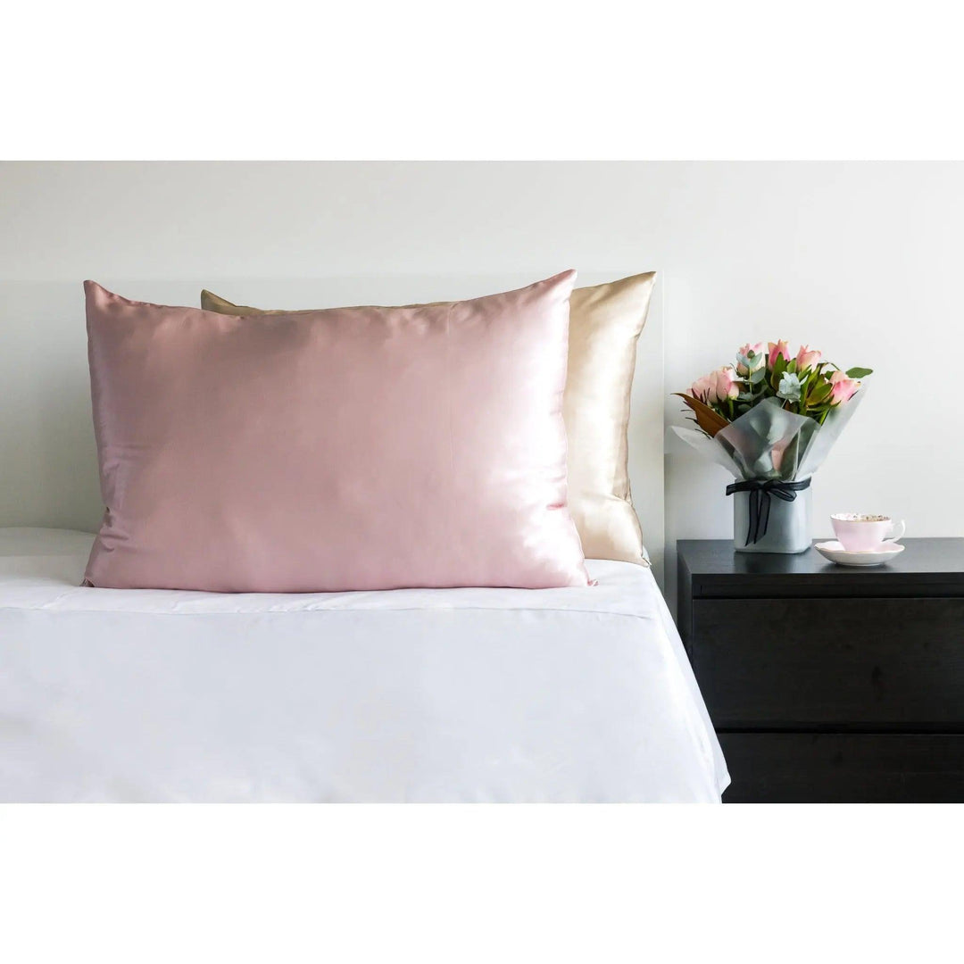 Pink Queen silk pillowcase displayed on a bed with beautiful flowers